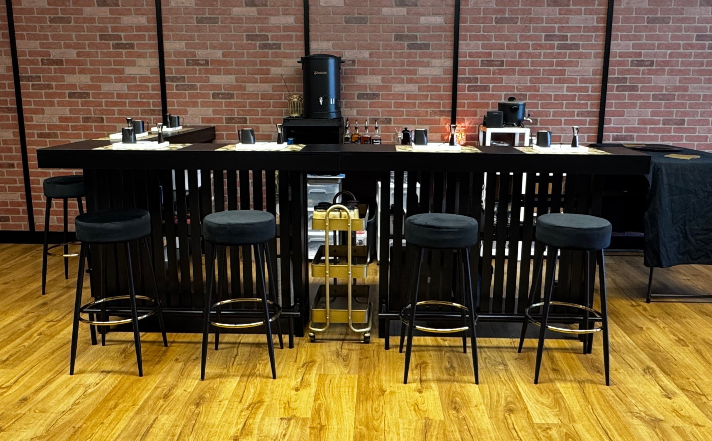 Bar area with black bar stools and counter against a brick wall.